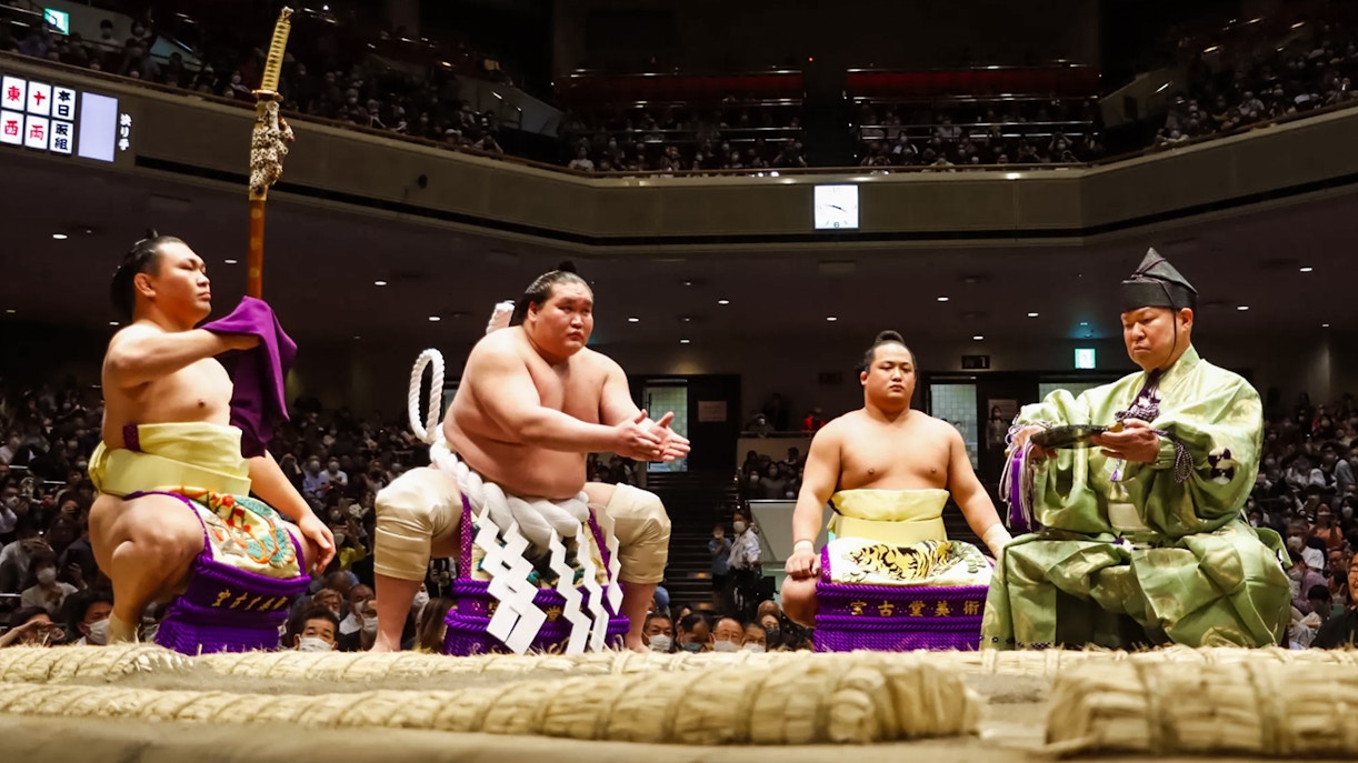 Sumo wrestlers and referee in traditional attire at Tokyo Grand Sumo Tournament.