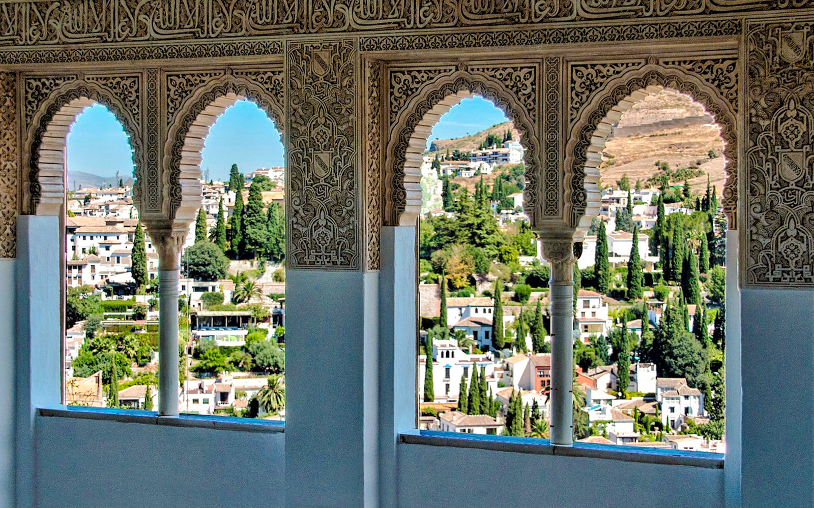 Arched windows with intricate carvings overlooking Granada from Alhambra fortress.