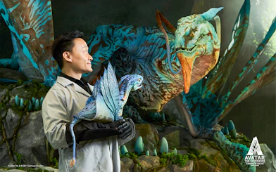 Man holding a small dragon-like creature with a larger one in the background at Gardens by the Bay, Singapore.