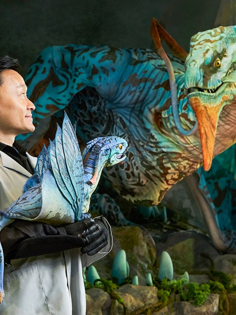 Man holding a small dragon-like creature with a larger one in the background at Gardens by the Bay, Singapore.