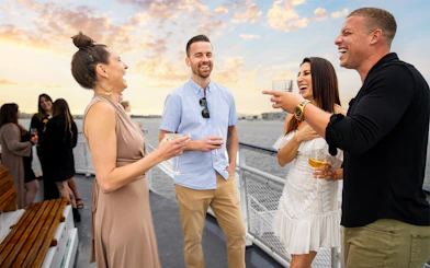 Guests enjoying drinks on the deck during sunset on the San Diego Signature Dinner Cruise.