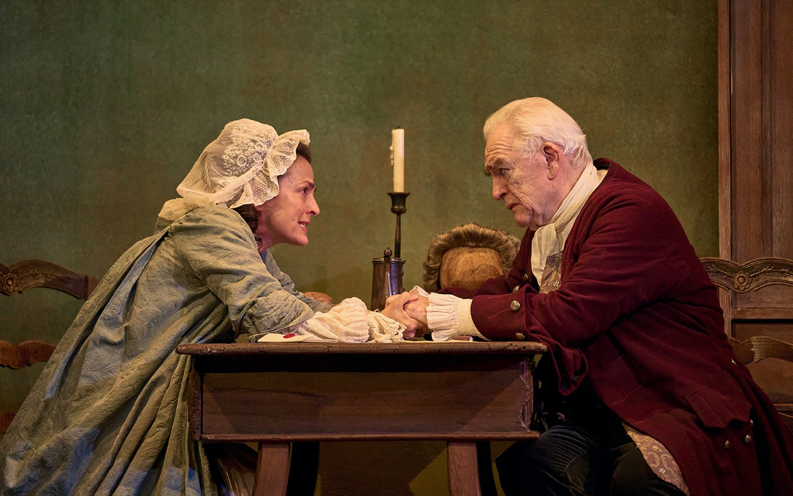 Two actors in period costumes perform an intense scene at a wooden table in "The Score" play.