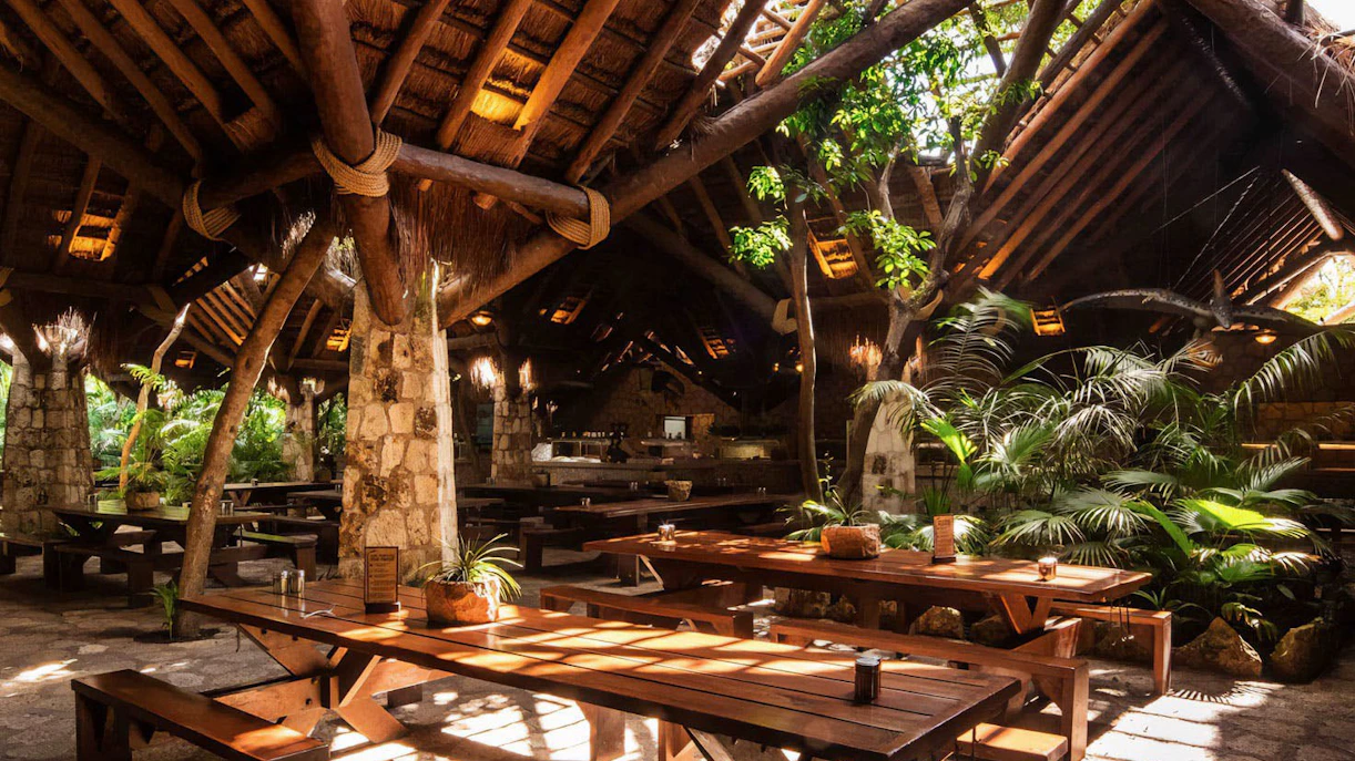 Rustic dining area with wooden tables and lush greenery at Xplor Park Restaurant.