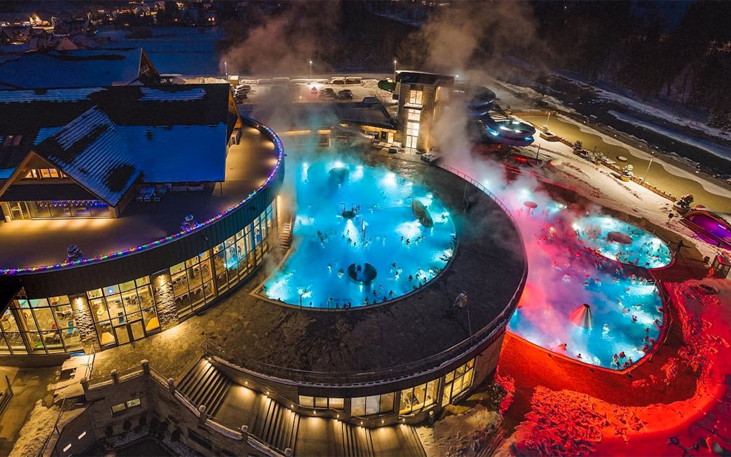 Thermal pools at night in Zakopane with steam rising, surrounded by snow.