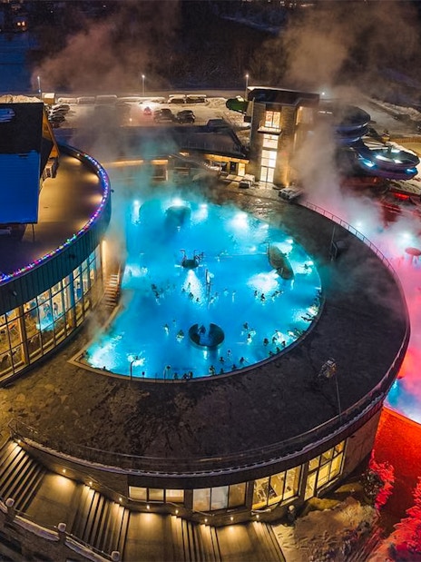 Thermal pools at night in Zakopane with steam rising, surrounded by snow.