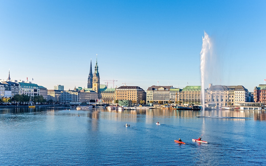 Hamburg cityscape with kayakers on Alster Lake and St. Nicholas' Church in view.