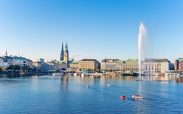 Hamburg cityscape with kayakers on Alster Lake and St. Nicholas' Church in view.