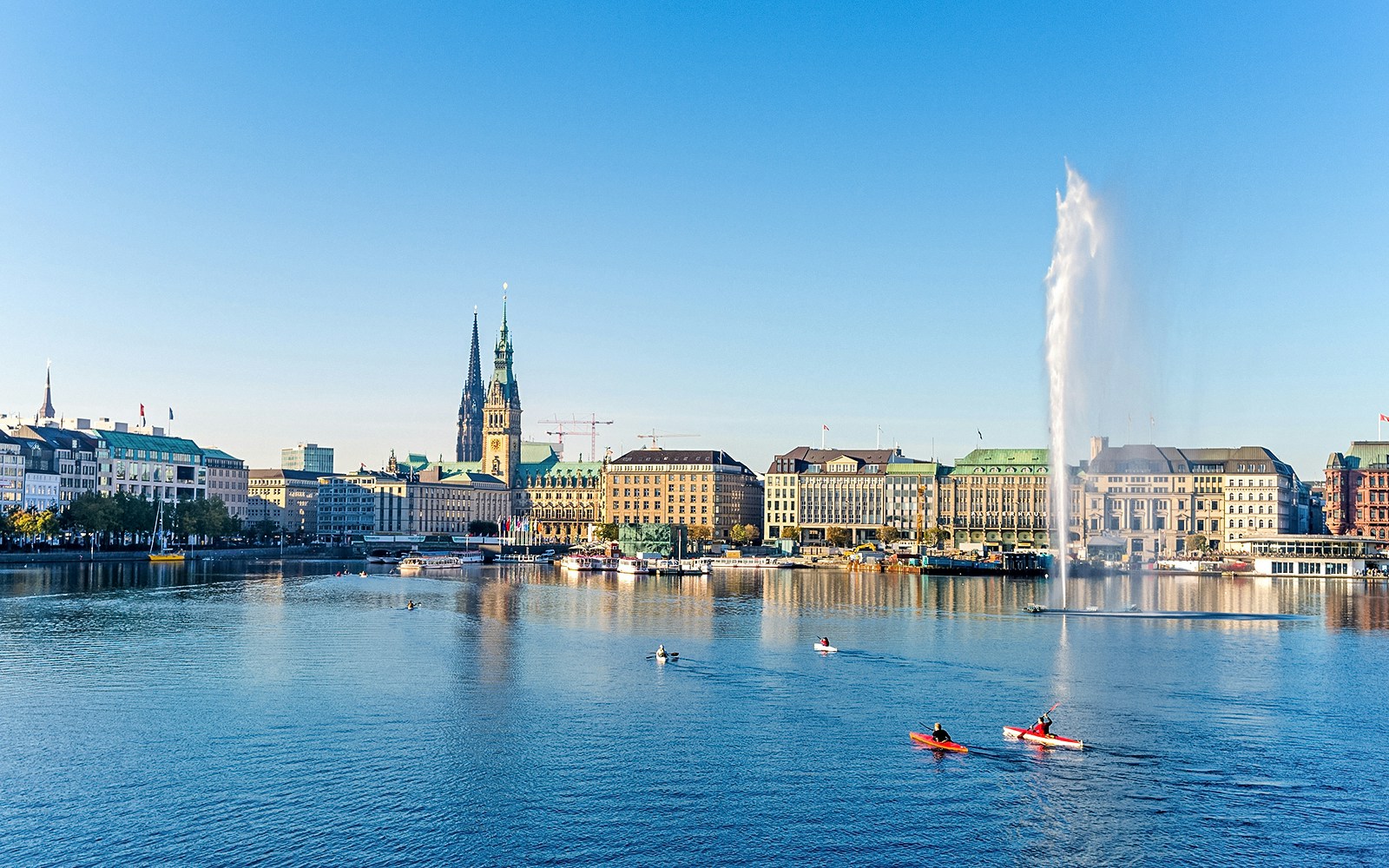 Hamburg cityscape with kayakers on Alster Lake and St. Nicholas' Church in view.