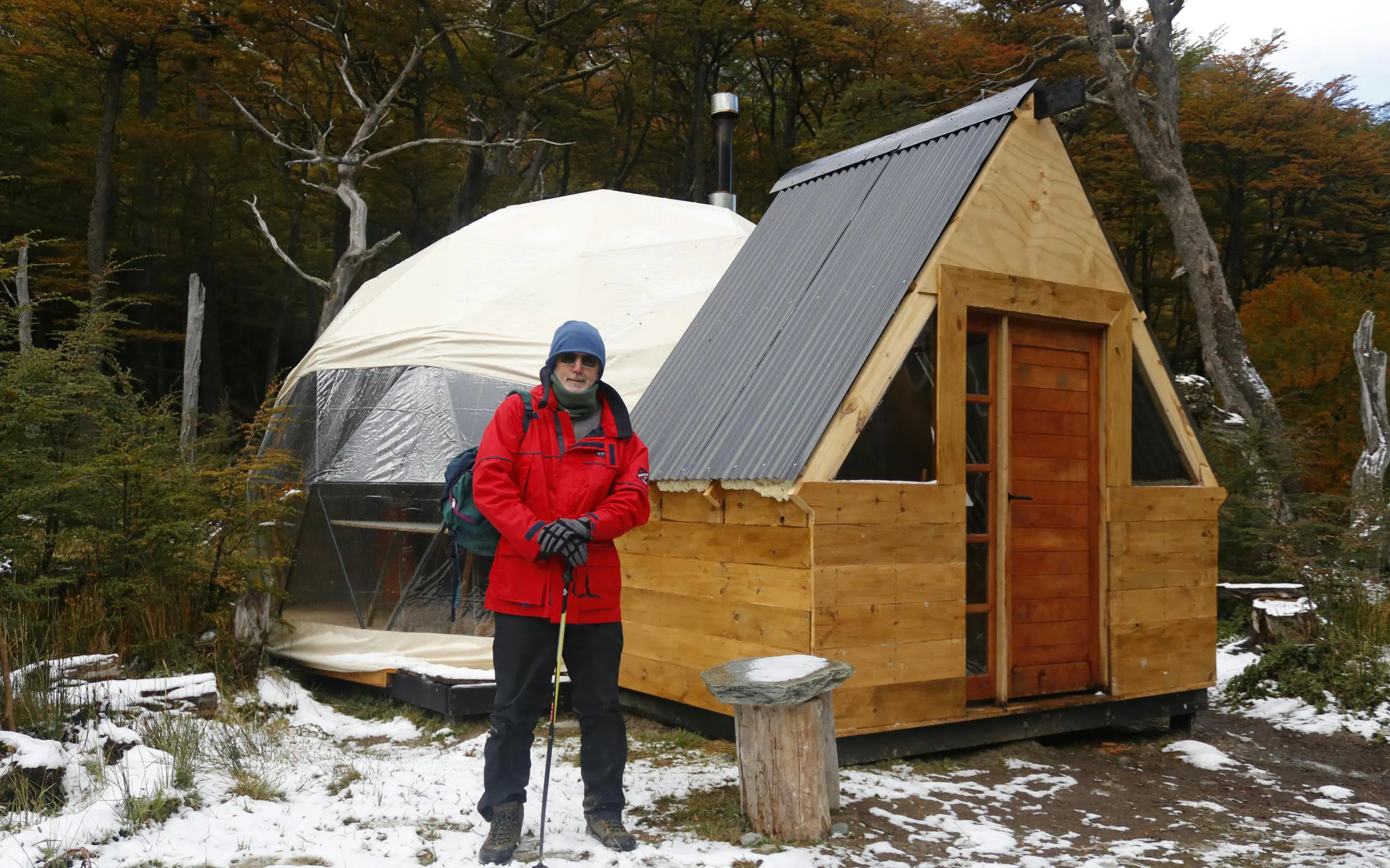 Trekker in red jacket at a wooden cabin near Esmeralda Lake, surrounded by snowy forest.
