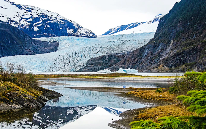 Mendenhall Glacier in Alaska with surrounding mountains and reflective lake.
