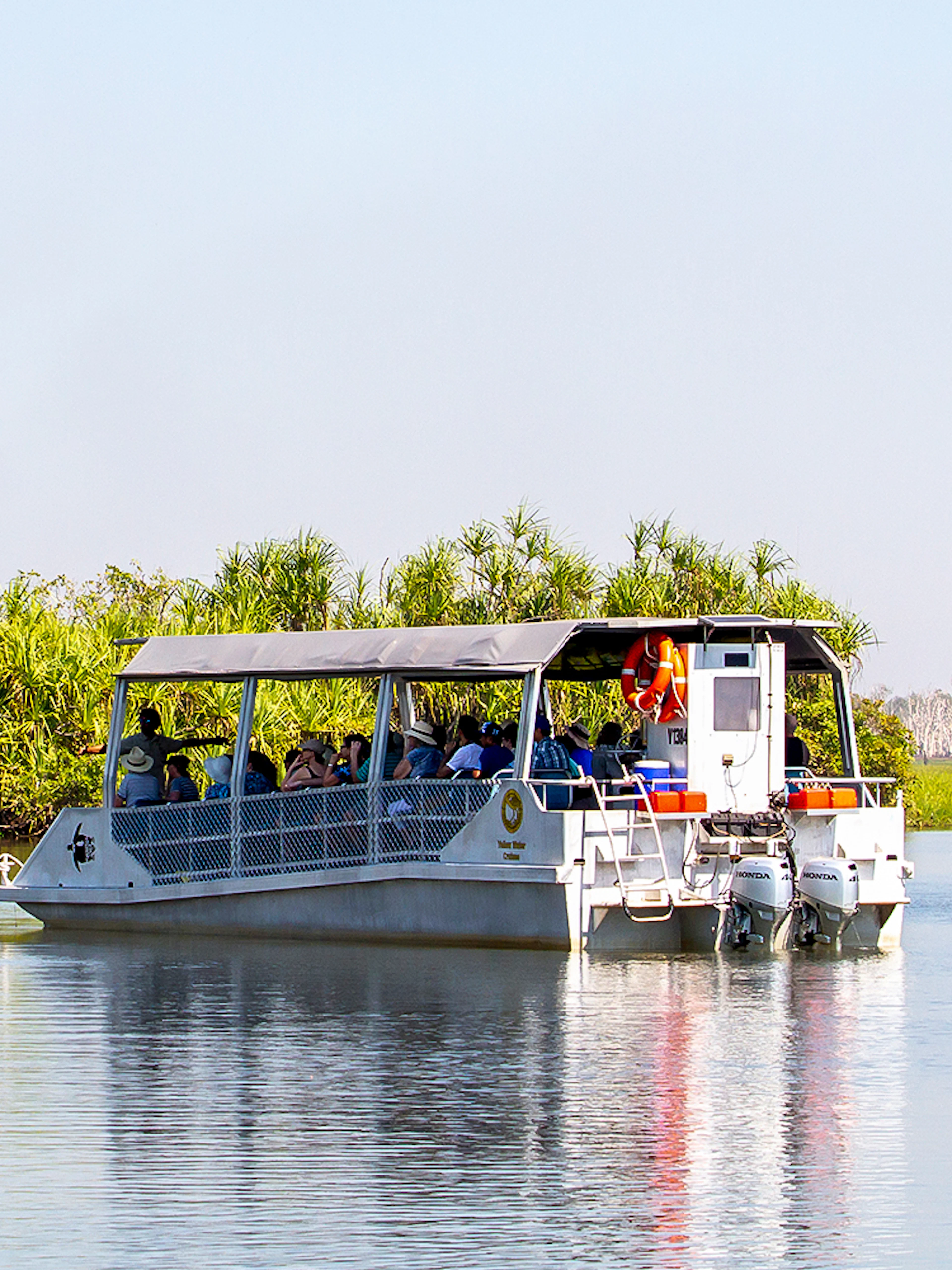 Tour boat cruising on Yellow Water Billabong in Kakadu National Park, surrounded by lush greenery.