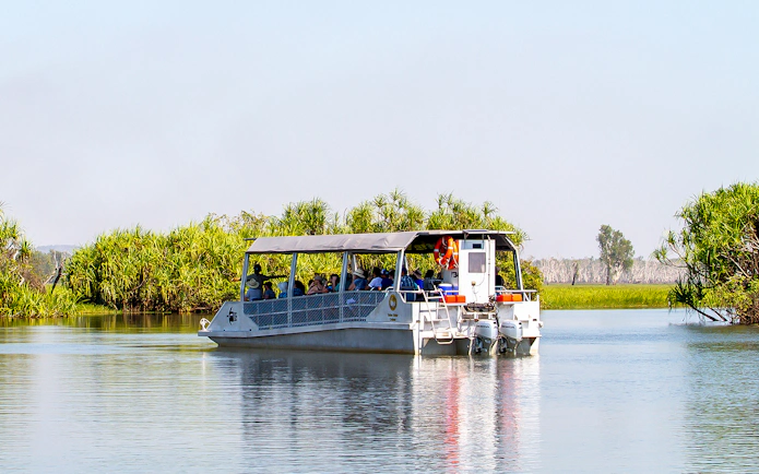 Tour boat cruising on Yellow Water Billabong in Kakadu National Park, surrounded by lush greenery.