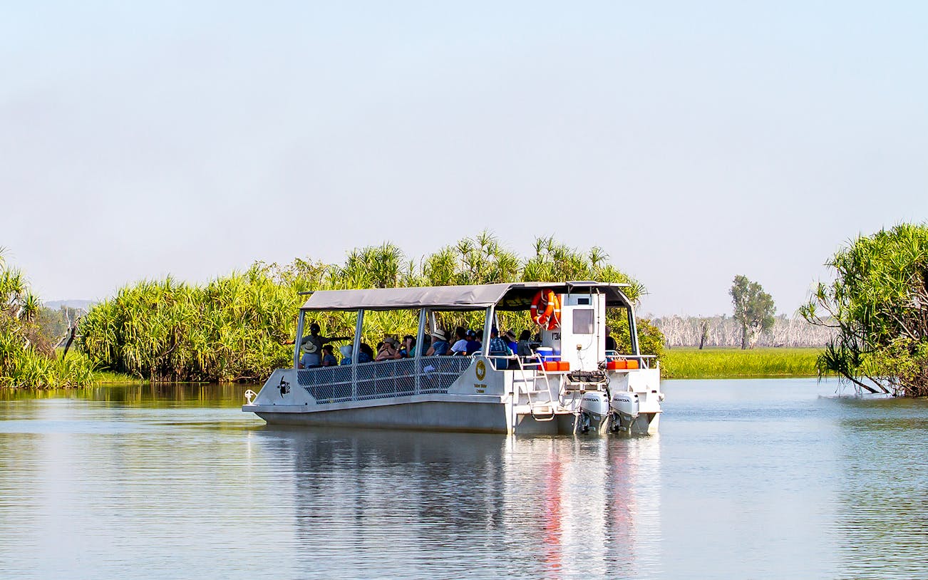 Tour boat cruising on Yellow Water Billabong in Kakadu National Park, surrounded by lush greenery.