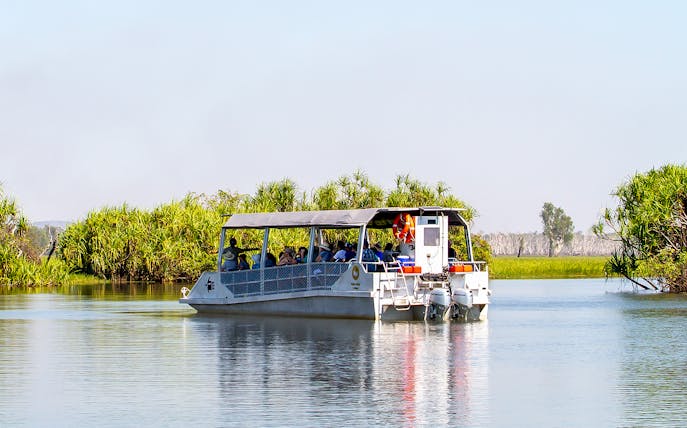 Tour boat cruising on Yellow Water Billabong in Kakadu National Park, surrounded by lush greenery.
