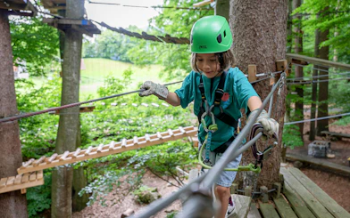 Child crossing rope bridge at Ropes Park Interlaken, wearing safety gear.