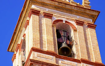 Bell tower of San Nicolás Church with brick details against blue sky.