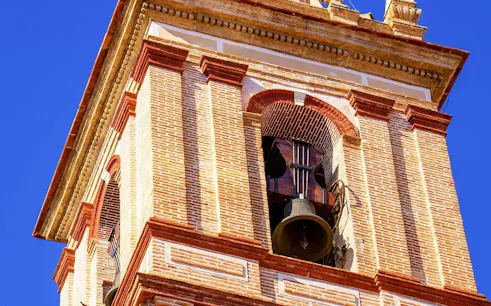 Bell tower of San Nicolás Church with brick details against blue sky.