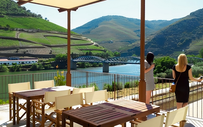 Tourists enjoying the view of Douro Valley vineyards and river from a terrace.