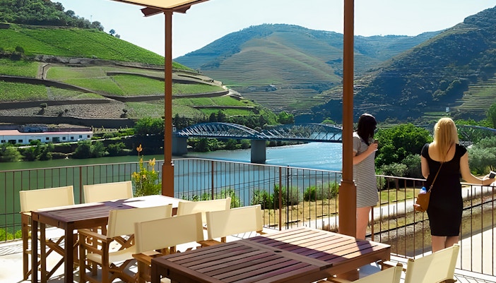 Tourists enjoying the view of Douro Valley vineyards and river from a terrace.