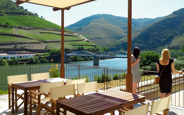 Tourists enjoying the view of Douro Valley vineyards and river from a terrace.