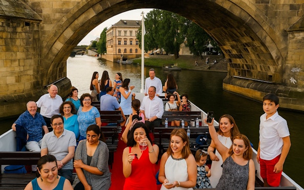 Guests enjoying a buffet dinner on a Prague evening cruise under a historic bridge.