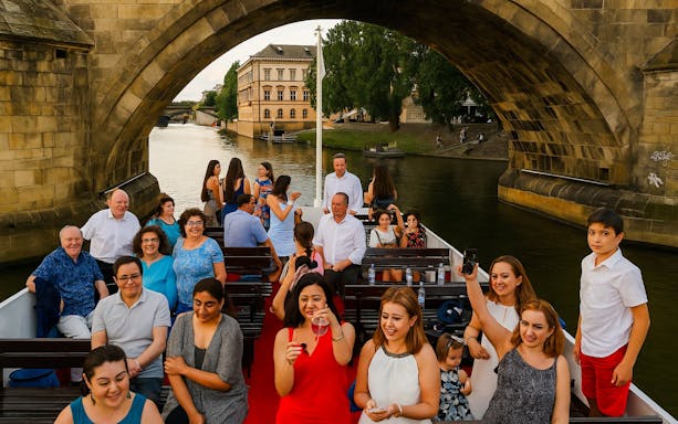 Guests enjoying a buffet dinner on a Prague evening cruise under a historic bridge.