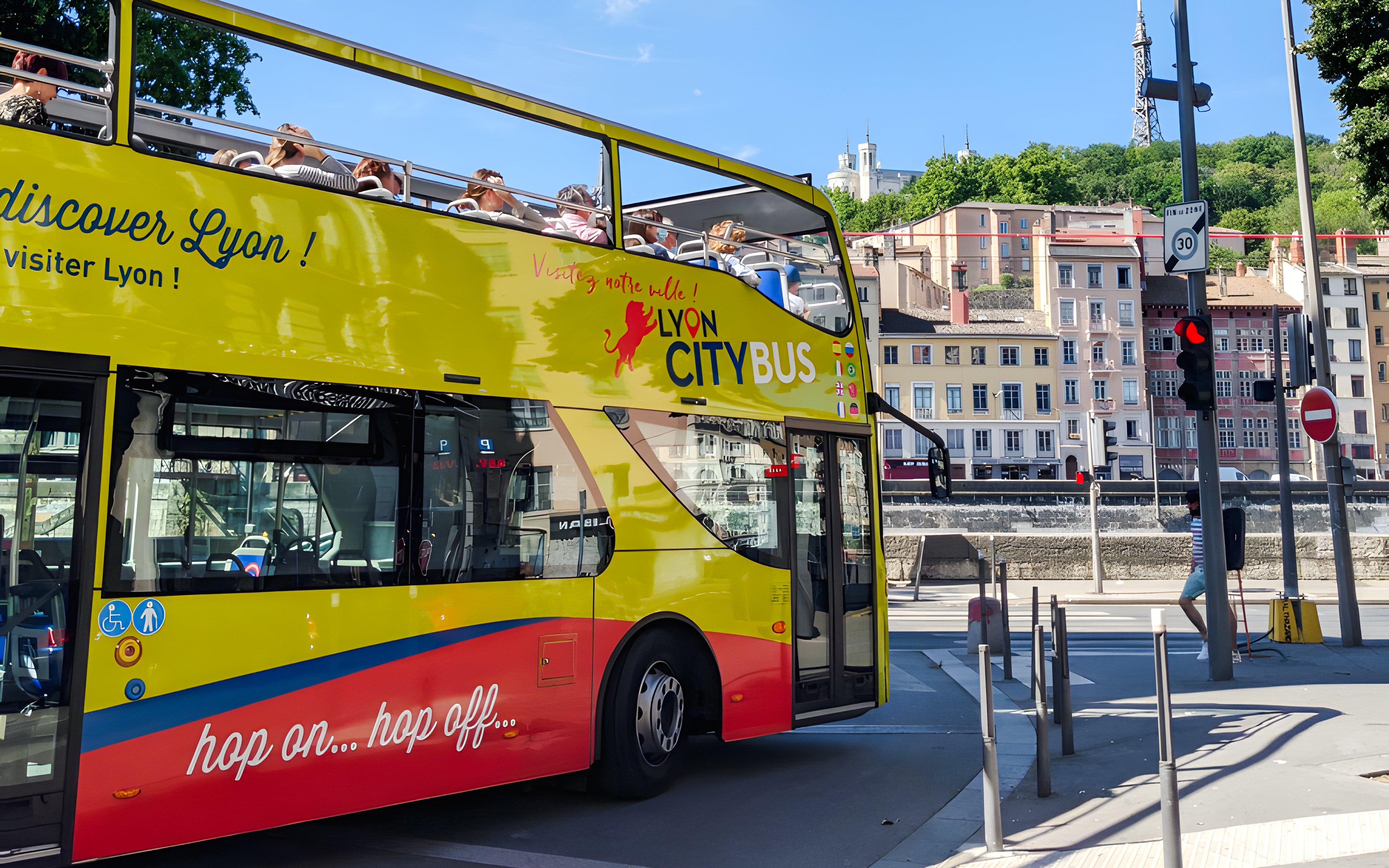 Lyon city tour bus with passengers, historic buildings in background, France.