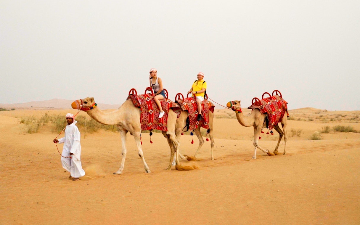 Camel ride during morning desert safari with guide in traditional attire.