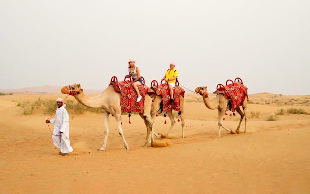 Camel ride during morning desert safari with guide in traditional attire.