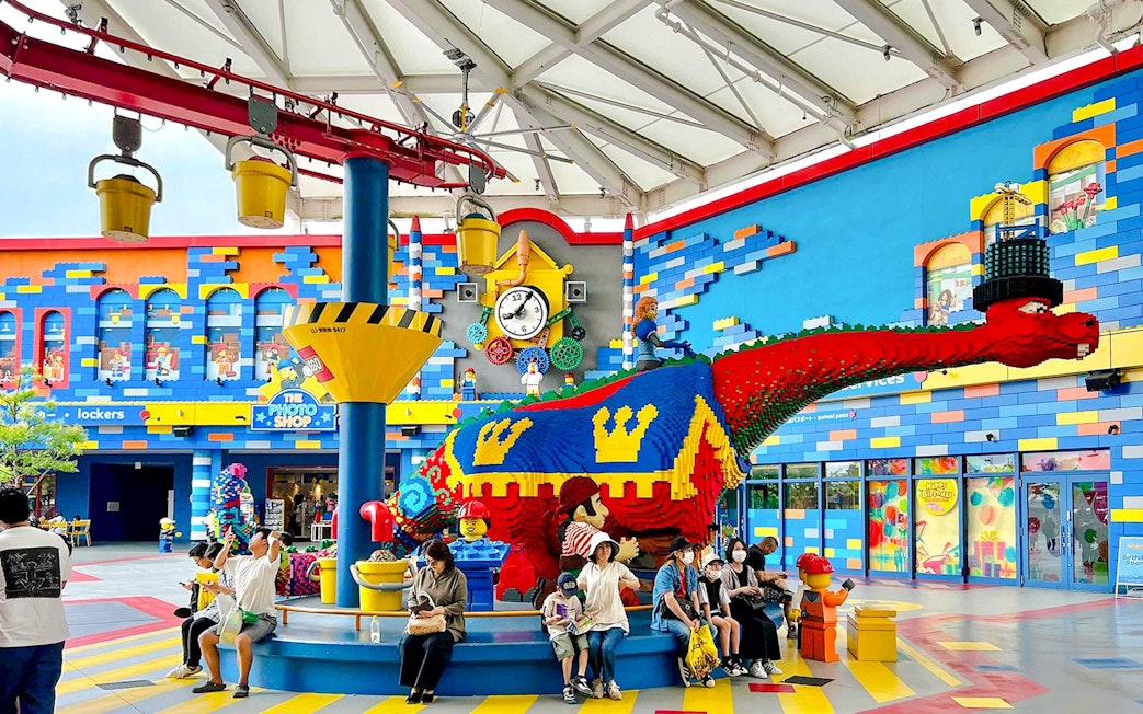 Colorful LEGO dinosaur sculpture at Legoland Japan with visitors seated nearby.