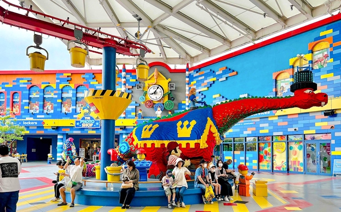 Colorful LEGO dinosaur sculpture at Legoland Japan with visitors seated nearby.