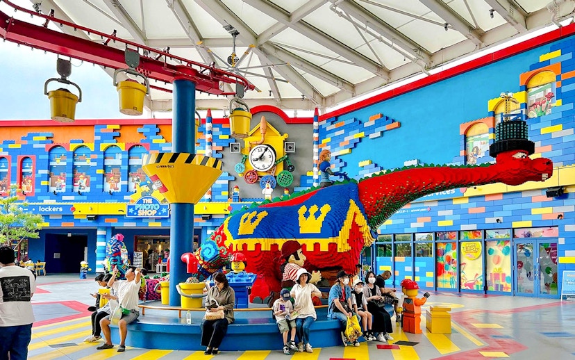 Colorful LEGO dinosaur sculpture at Legoland Japan with visitors seated nearby.