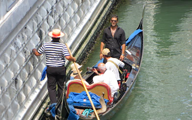 Gondolier steering a gondola with passengers enjoying a serenade in Venice canal.