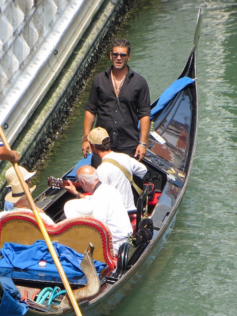 Gondolier steering a gondola with passengers enjoying a serenade in Venice canal.