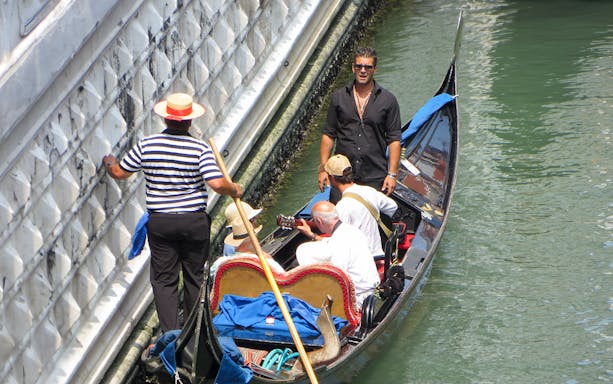 Gondolier steering a gondola with passengers enjoying a serenade in Venice canal.