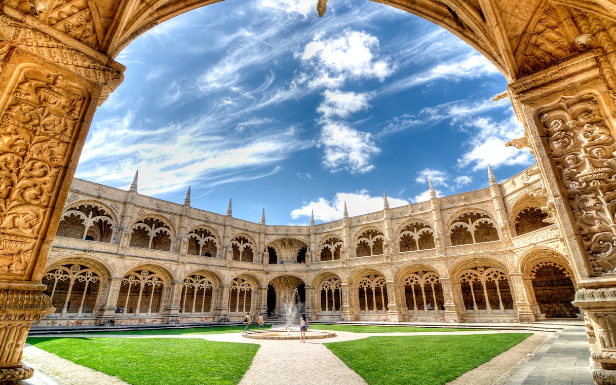 Cloister of Jeronimos Monastery in Lisbon with ornate arches and central fountain.