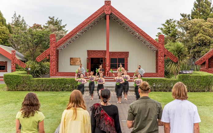 Maori cultural performance at Te Puia, New Zealand, with traditional meeting house in background.
