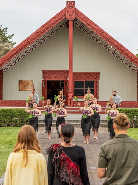 Maori cultural performance at Te Puia, New Zealand, with traditional meeting house in background.