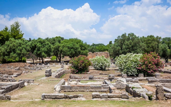 Ancient ruins surrounded by trees and flowers at the Archaeological Site of Olympia, Greece.