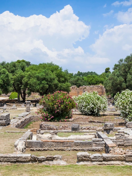 Ancient ruins surrounded by trees and flowers at the Archaeological Site of Olympia, Greece.