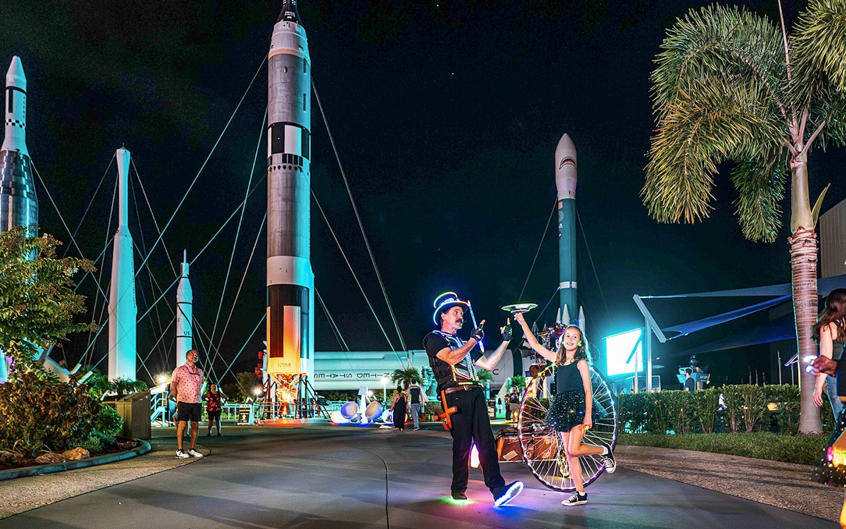 Performer and child with glowing props at Kennedy Space Center after-hours event.