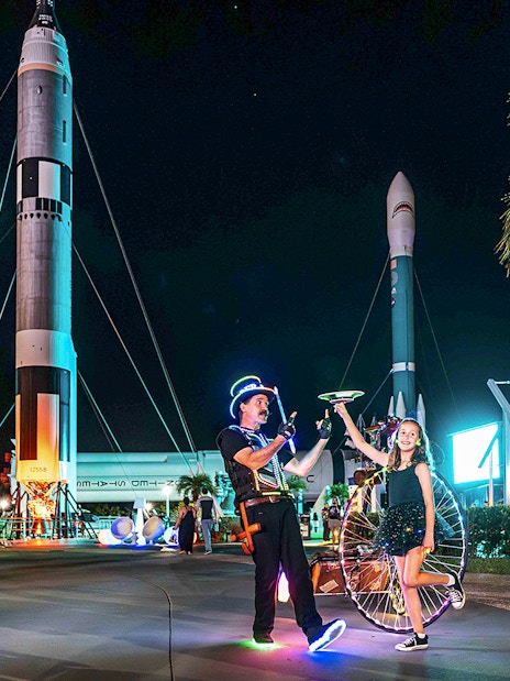 Performer and child with glowing props at Kennedy Space Center after-hours event.