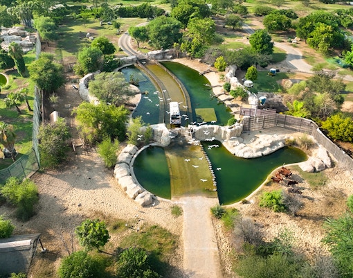 Aerial view of Dubai Safari Park with lush greenery, water features, and a safari vehicle.