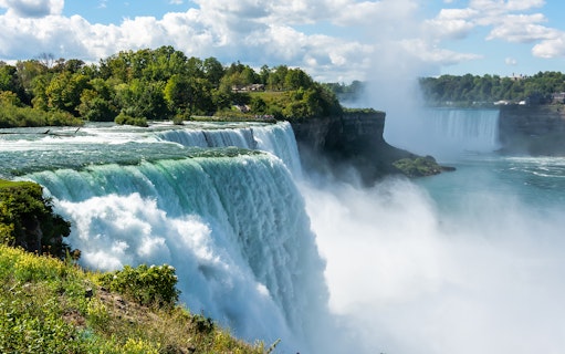 Bridal Veil Falls cascading into the Niagara River surrounded by lush greenery.