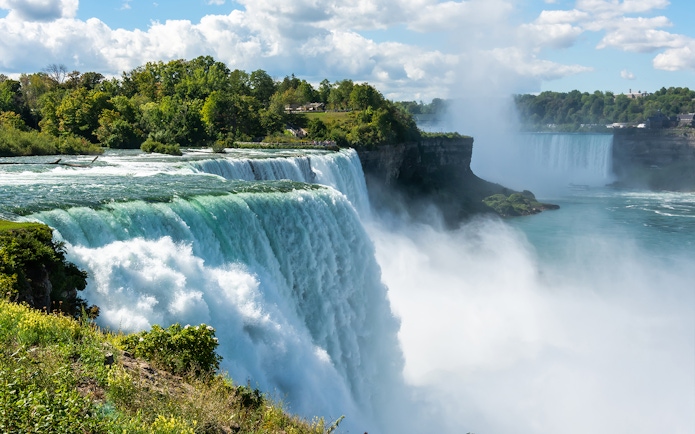 Bridal Veil Falls cascading into the Niagara River surrounded by lush greenery.