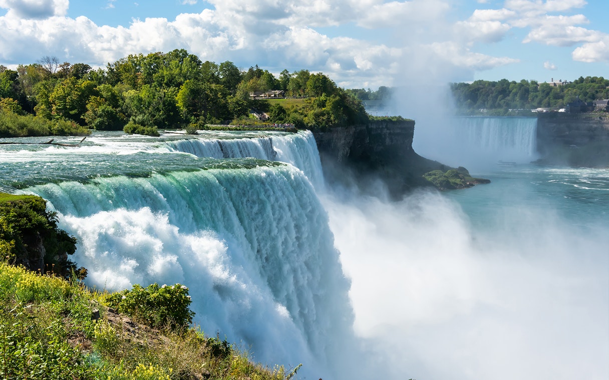 Bridal Veil Falls cascading into the Niagara River surrounded by lush greenery.