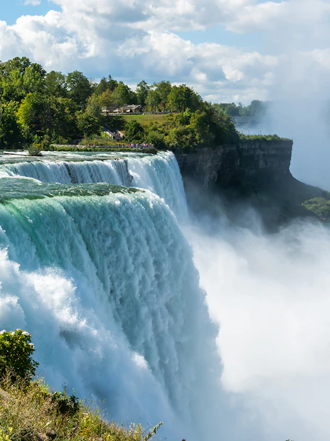 Bridal Veil Falls cascading into the Niagara River surrounded by lush greenery.