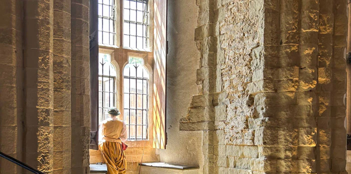 Person in historical attire looking out a window inside the White Tower, London.