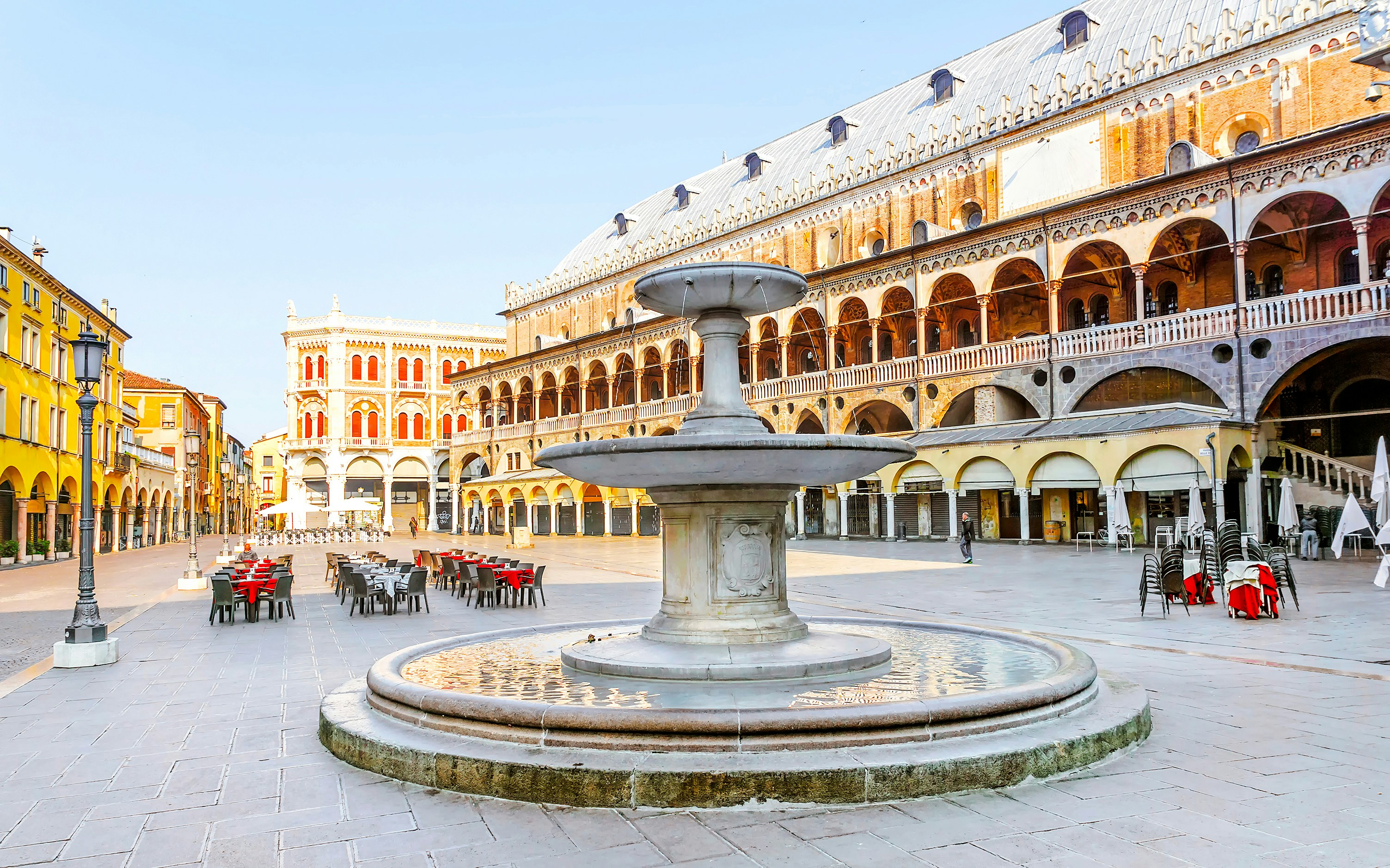 Fountain in Piazza delle Erbe, Padua, with historic buildings and outdoor seating.