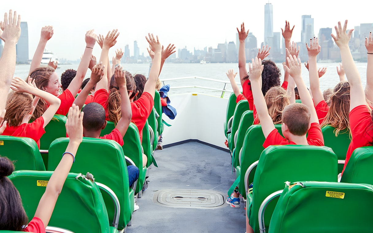 Guests raising hands on NYC speedboat ride with city skyline in view.